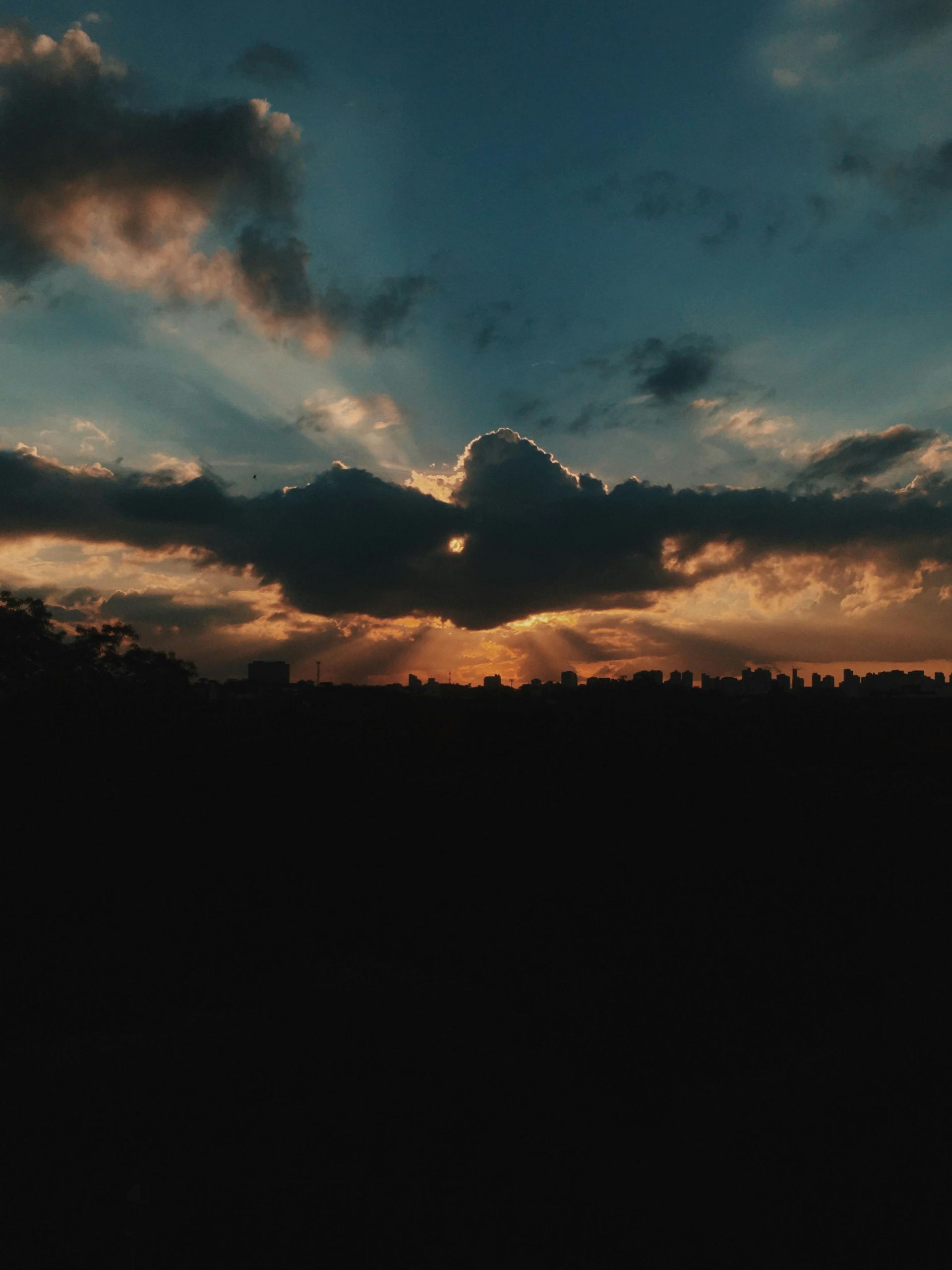 Dark cloudy sunset over a silhouetted horizon with orange light breaking through.