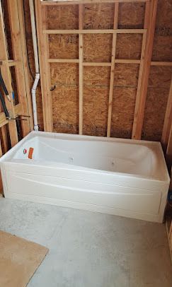 A white jetted bathtub installed in a bathroom under construction with exposed wooden wall studs and concrete flooring.