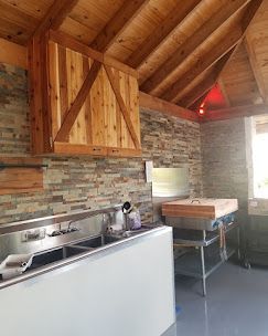 A rustic kitchen with wood-paneled walls and ceilings, a stone backsplash, a stainless steel sink, and a wooden hood.