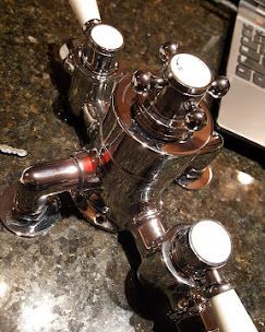 Chrome bathroom faucet with a central temperature control dial, lever handles, and white accents on a dark stone counter.
