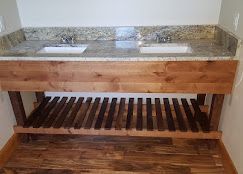 A double-sink bathroom vanity with a granite countertop, wooden base, and slatted lower shelf.