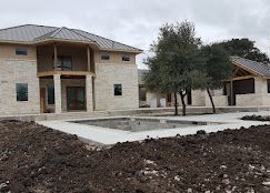 A newly built two-story stone house with a metal roof, featuring a pool deck and unfinished landscaping in the foreground.