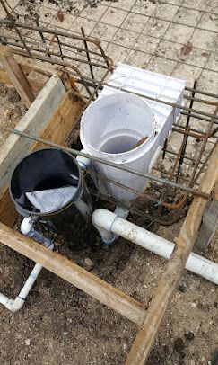 Plumbing pipes and a white floor drain installation set within a wooden frame and metal rebar at a construction site.
