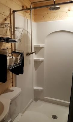 A rustic bathroom featuring a white shower stall with built-in shelving, an exposed shower head, and wall-mounted baskets.