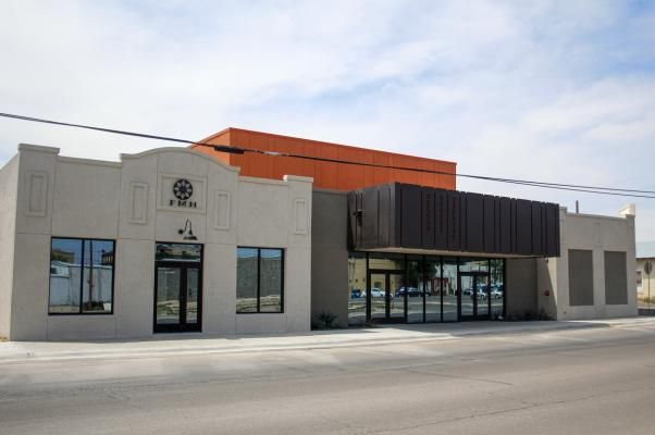 A modern building with a light-colored stucco facade, a dark metal entrance canopy, and an orange upper structure.