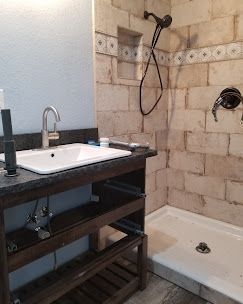 A bathroom vanity with a white sink next to a stone-tiled walk-in shower with a handheld showerhead.