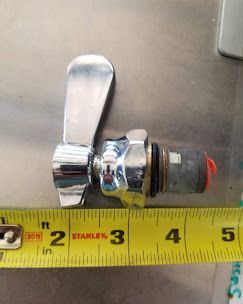 A chrome faucet cartridge handle next to a yellow Stanley tape measure on a metal surface, measuring about 3.5 inches.