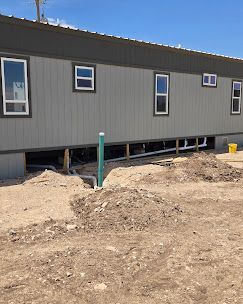 A tan manufactured home under construction with exposed plumbing pipes and piles of dirt on a clear day.