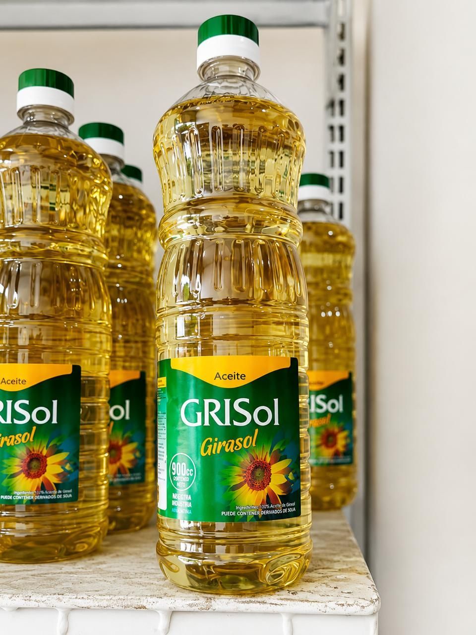 Fila de botellas transparentes de aceite de cocina amarillo con tapones y etiquetas verdes en un estante de la tienda.