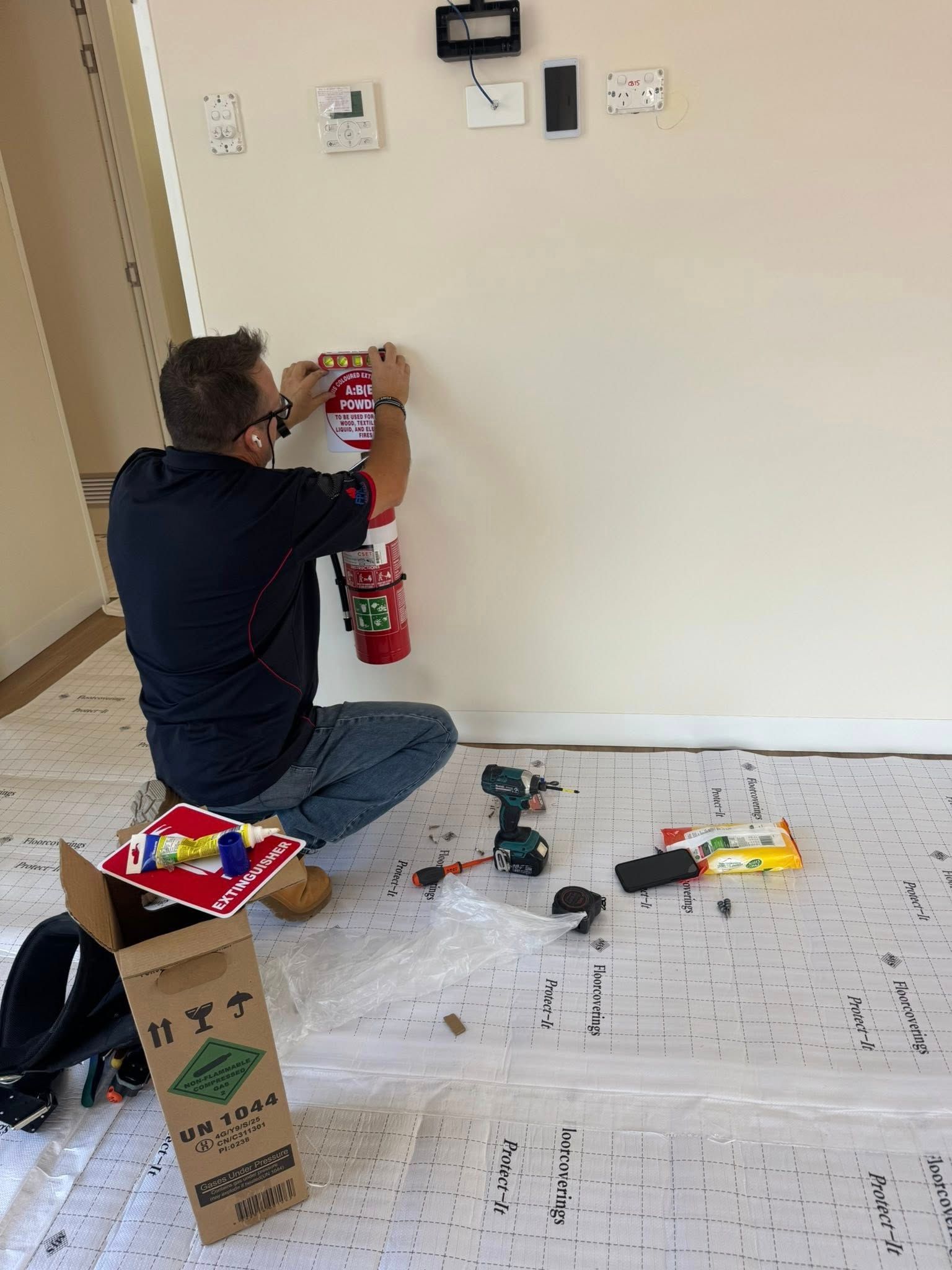 MAN Kneels Beside a Wall-mounted Fire Extinguisher, Installing — CSET Group Fire & Security in Central Coast, NSW