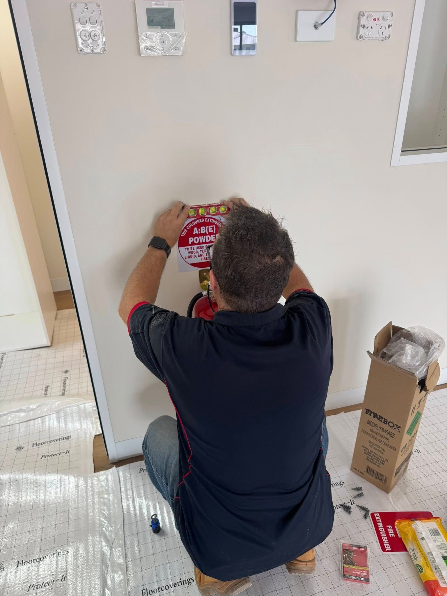 Person Kneeling on a Carpet, Hanging a Red Item on a Wall in a Room — CSET Group Fire & Security in Lake Macquarie, NSW