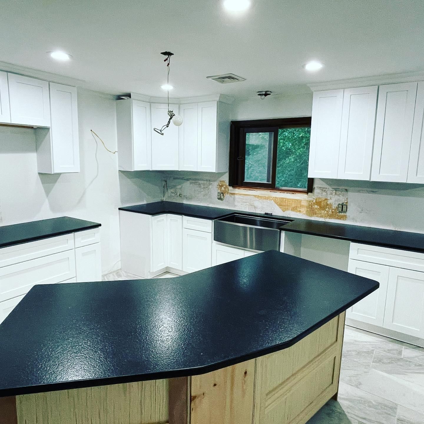 White kitchen cabinets with black countertops and wood island.
