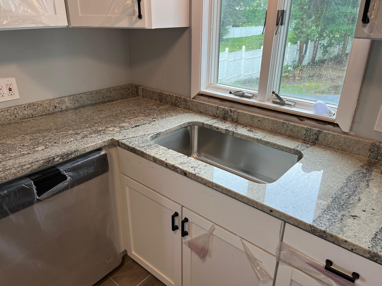 Corner kitchen with granite countertop, stainless steel sink, white cabinets, and a window.