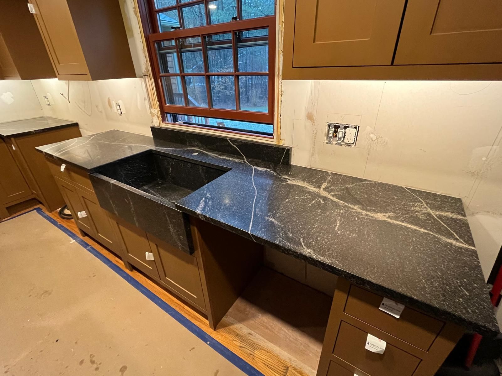 Kitchen with brown cabinets and a black countertop, featuring a farmhouse sink and window.