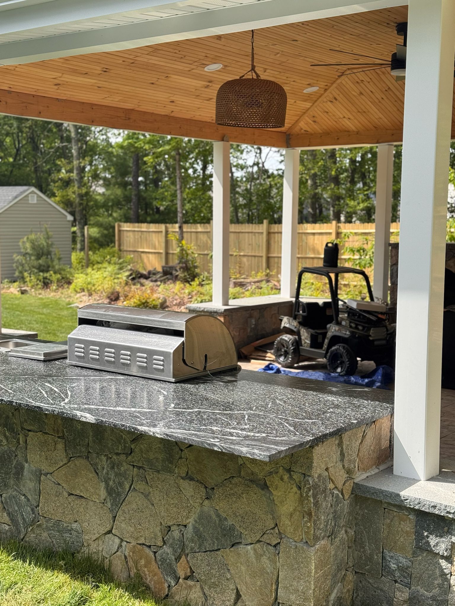 Outdoor kitchen with stone base and granite countertop, under a covered patio.