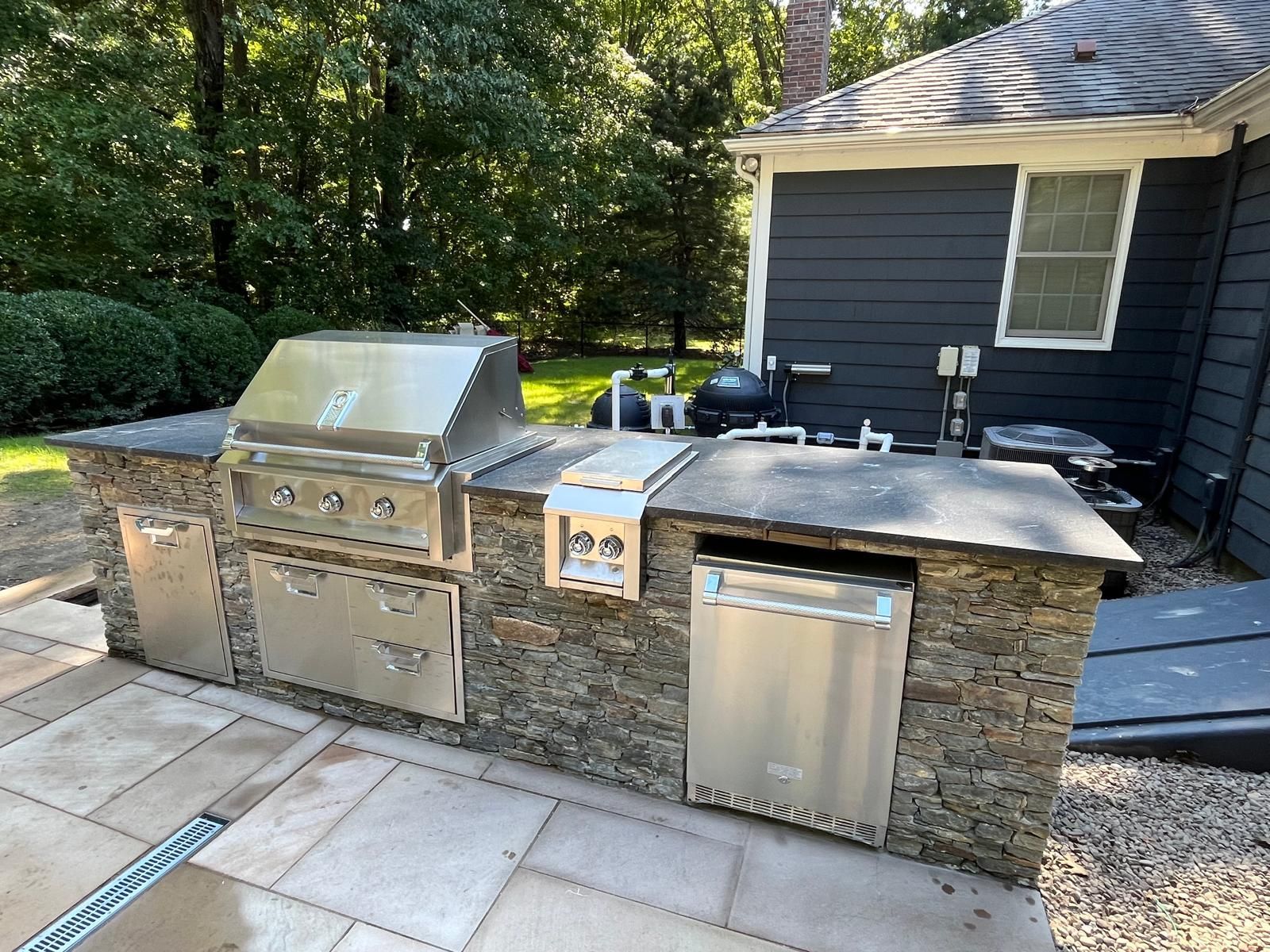 Outdoor kitchen with stainless steel appliances and stone facade on a patio.