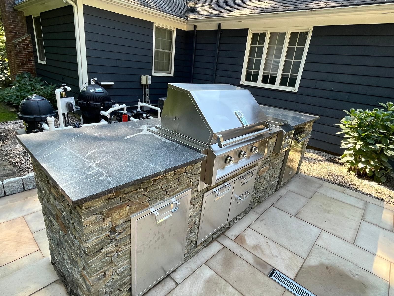 Outdoor kitchen with stainless steel grill, stone countertop and facade, and built-in storage.