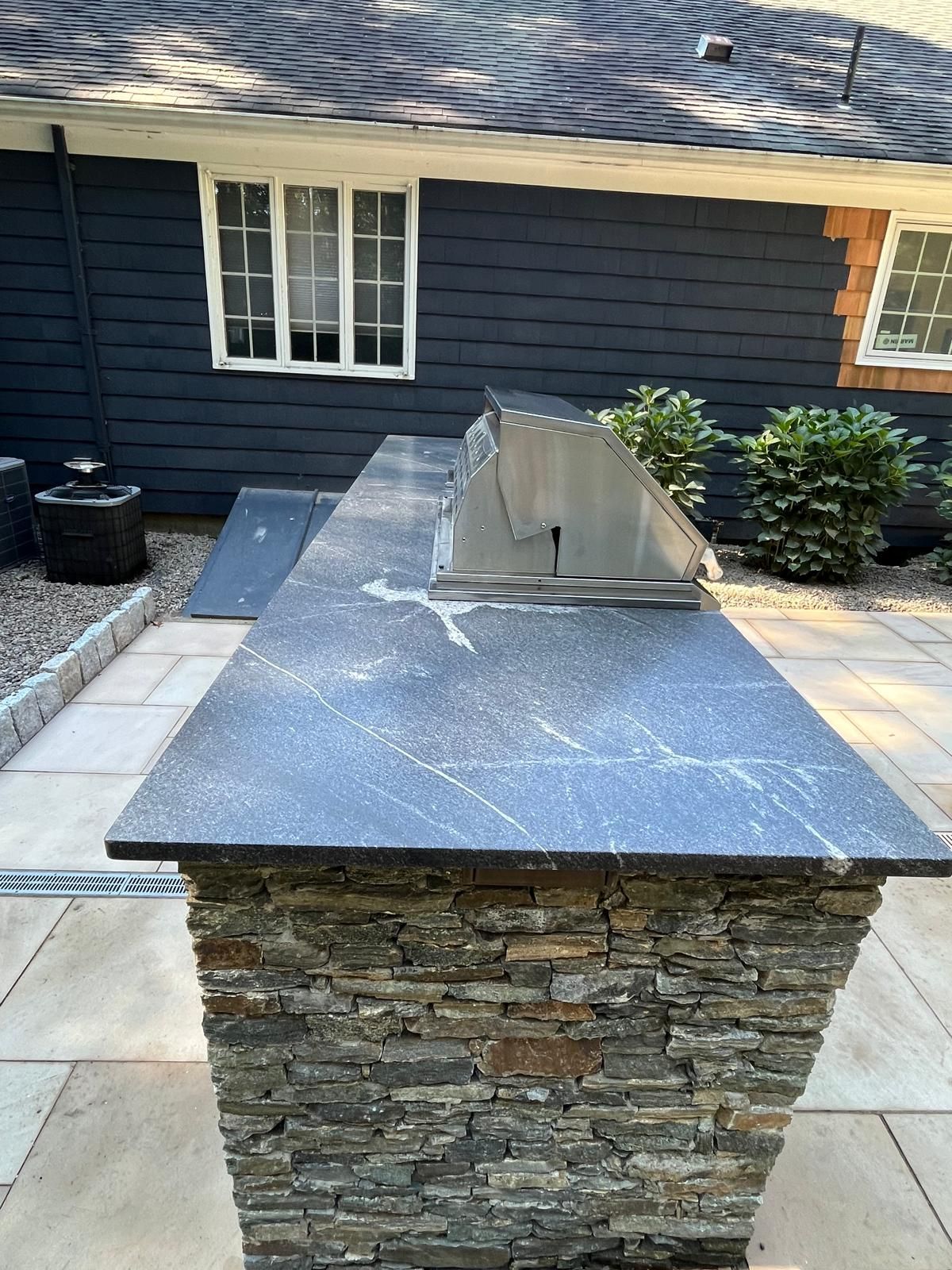 Outdoor kitchen island with a stone base and black countertop; grill built-in.