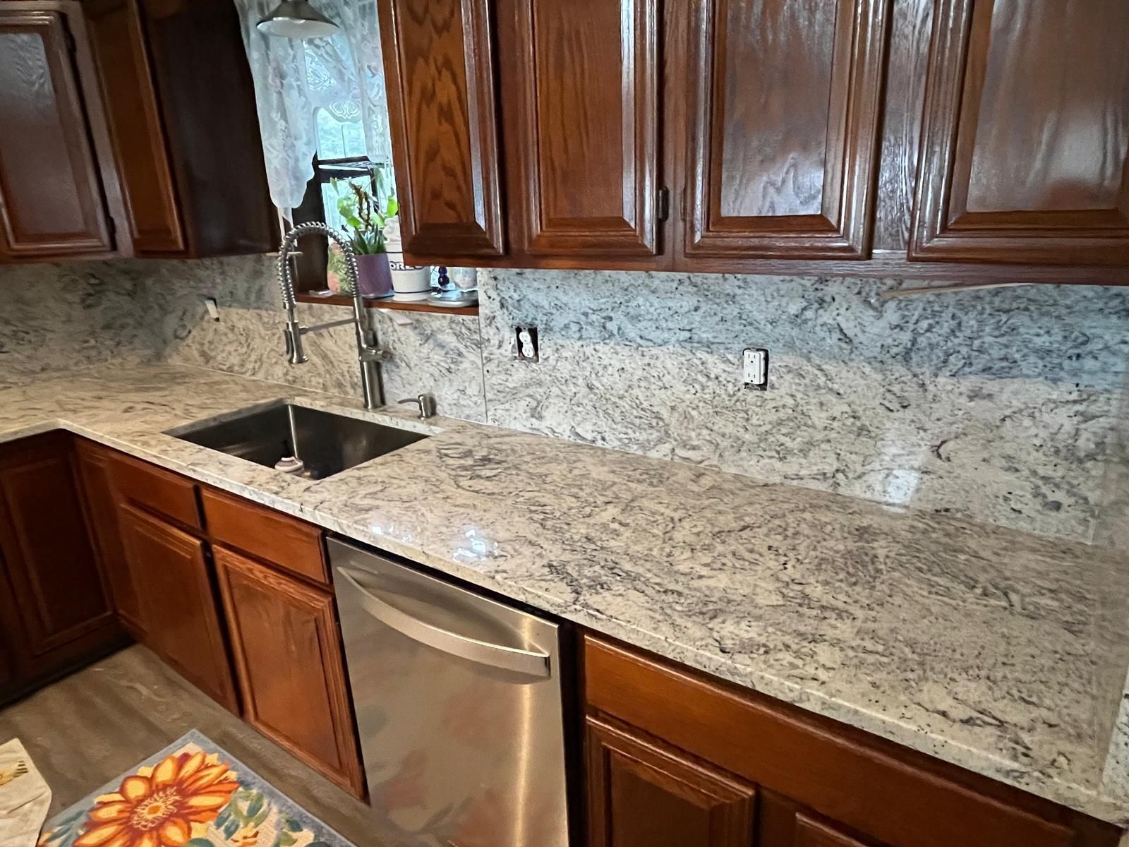 Kitchen with granite countertops and dark wooden cabinets, with a sink and a stainless steel dishwasher.