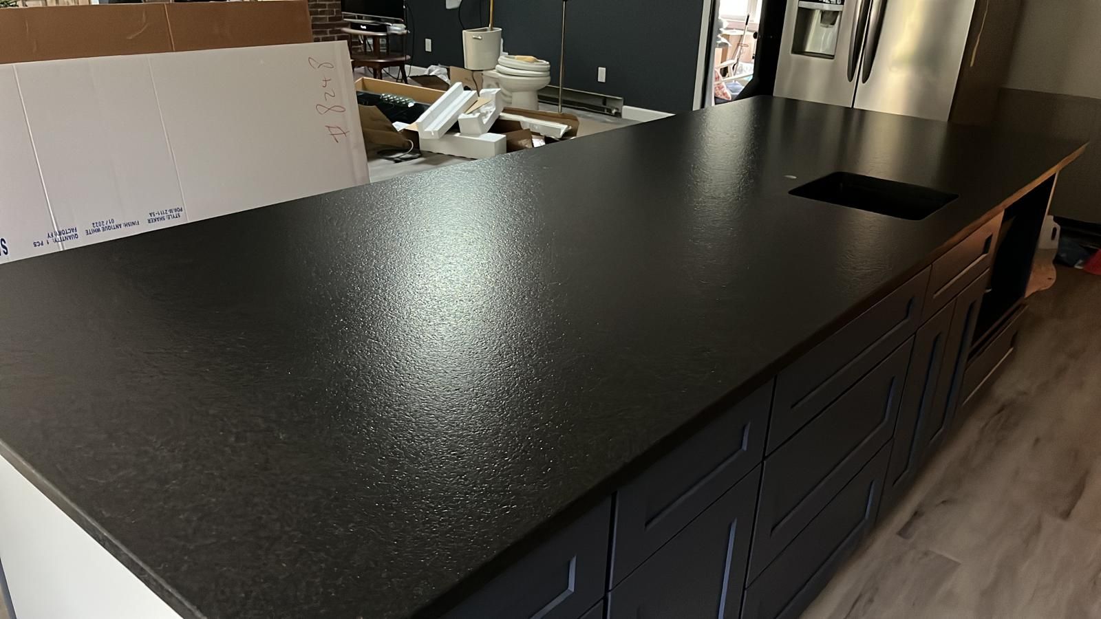 Black countertop on dark cabinets, with a sink, in a kitchen.
