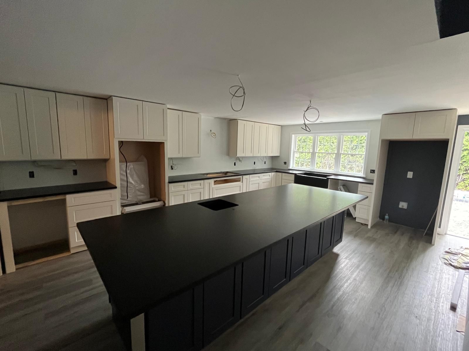 Kitchen with black island, white cabinets, and gray flooring; under construction.