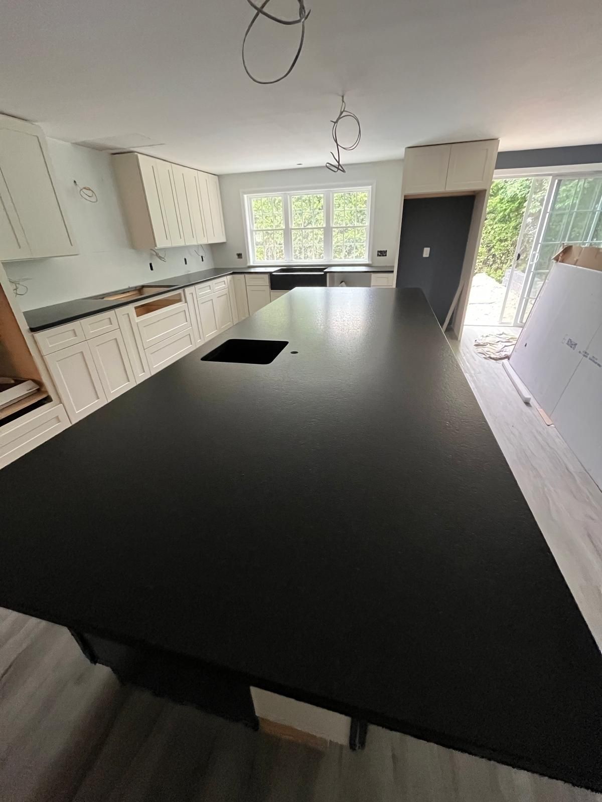 Newly installed black countertop in a modern kitchen with white cabinets and a window.