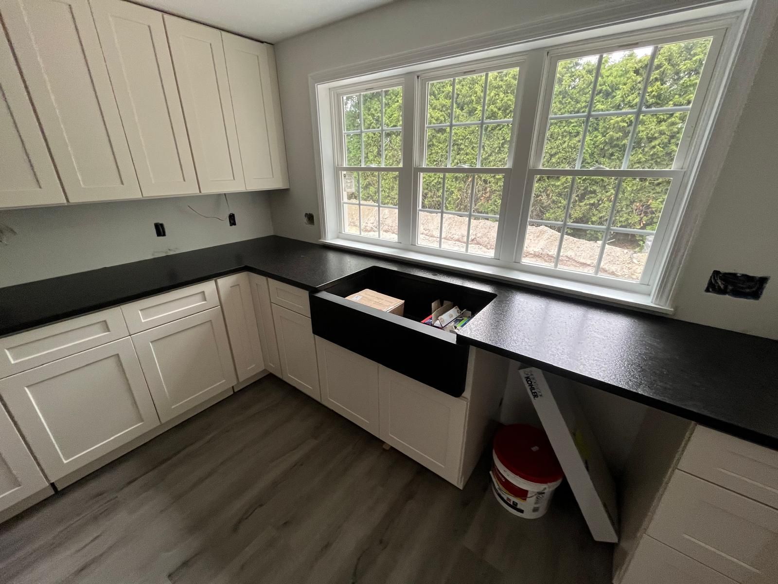 Cream-colored kitchen cabinets with a black countertop and a black farmhouse sink under a window.