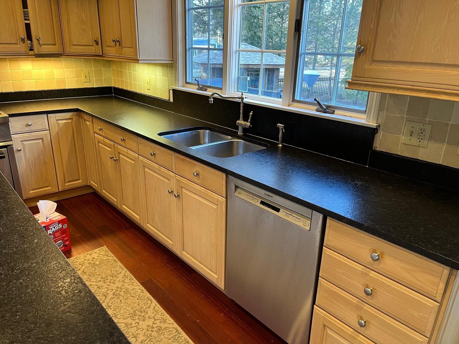 Kitchen with light wood cabinets, black countertops, stainless steel appliances, and a window.