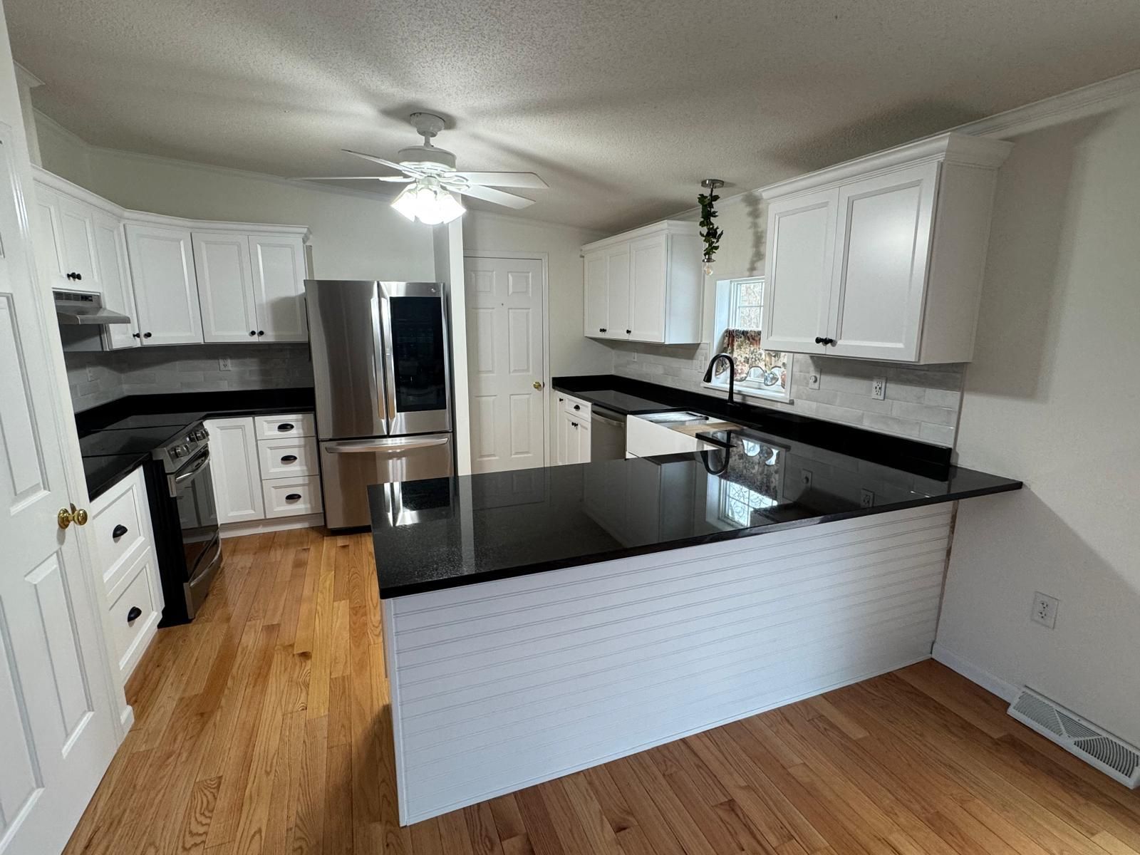 Bright kitchen with white cabinets, black countertops, and wood floors.