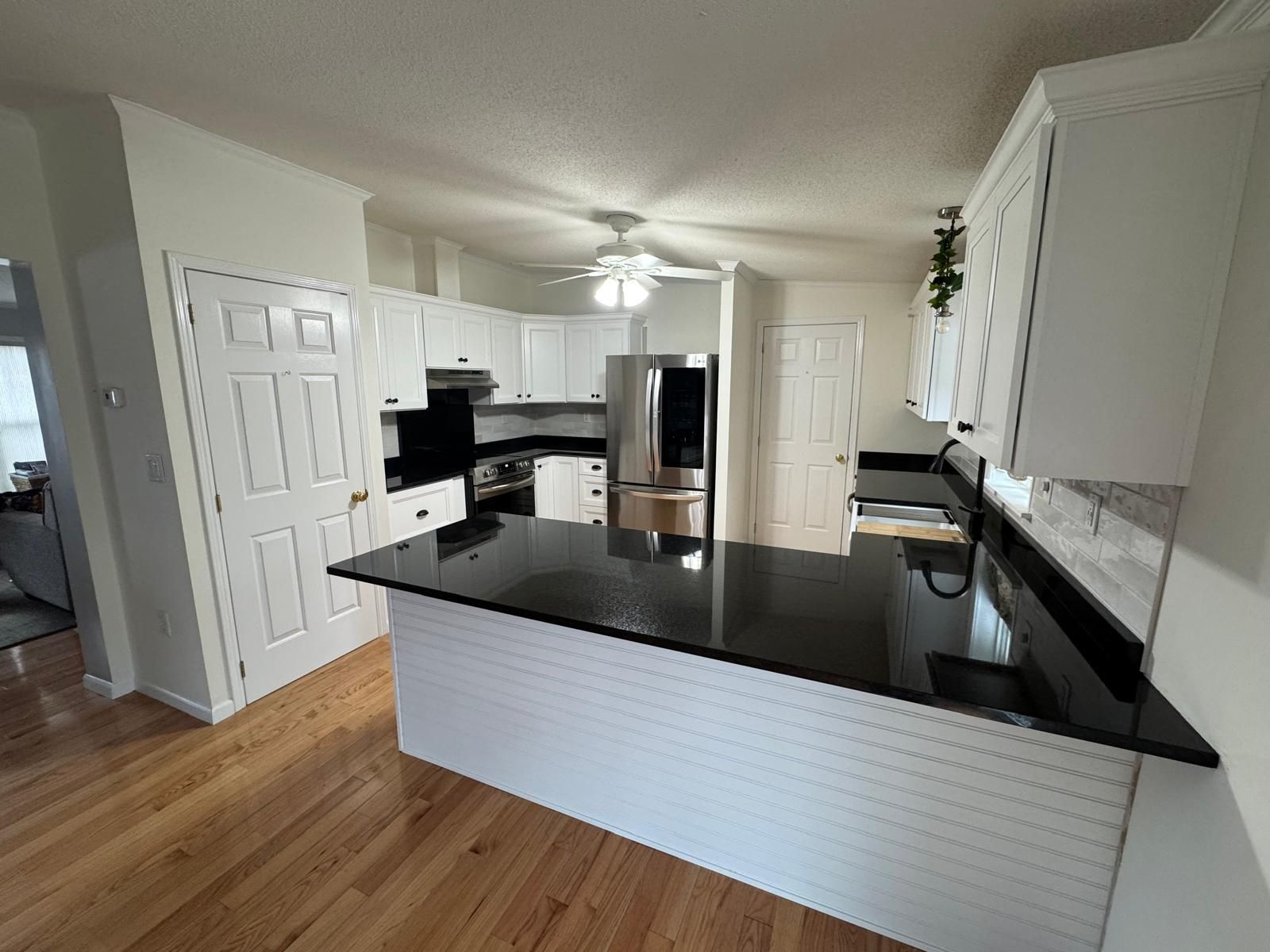 White kitchen with black countertops, wood floors, and white backsplash.