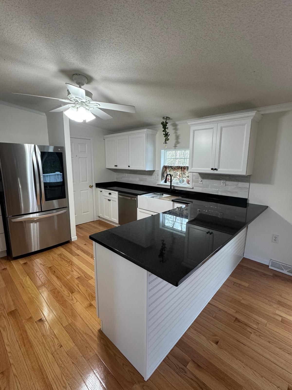 Kitchen with white cabinets, black countertops, stainless steel appliances, and wooden floors.