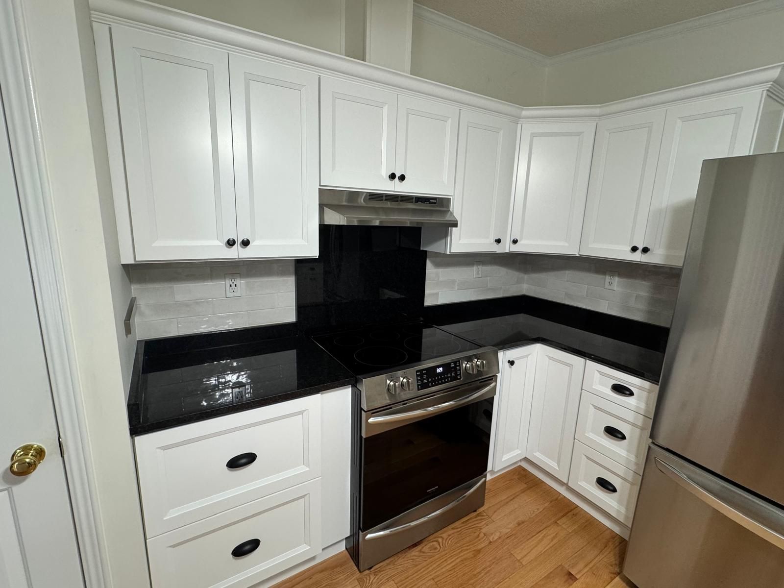White kitchen cabinets, black countertops, stainless steel appliances, and wood flooring.