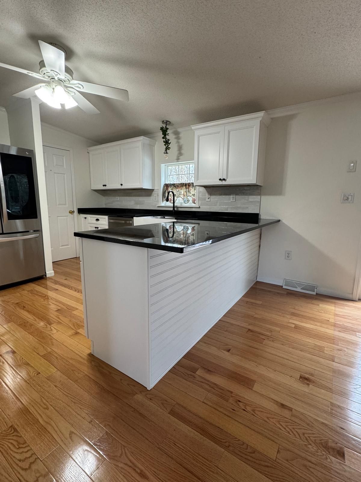 Kitchen with white cabinets, black countertops, and a white island on wooden floors.