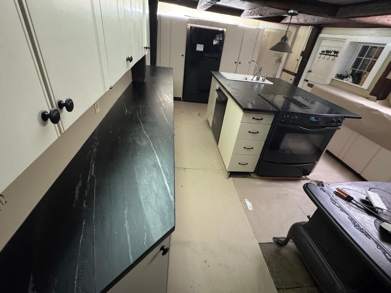 Kitchen with white cabinets, black countertops, island with an oven, and black door.
