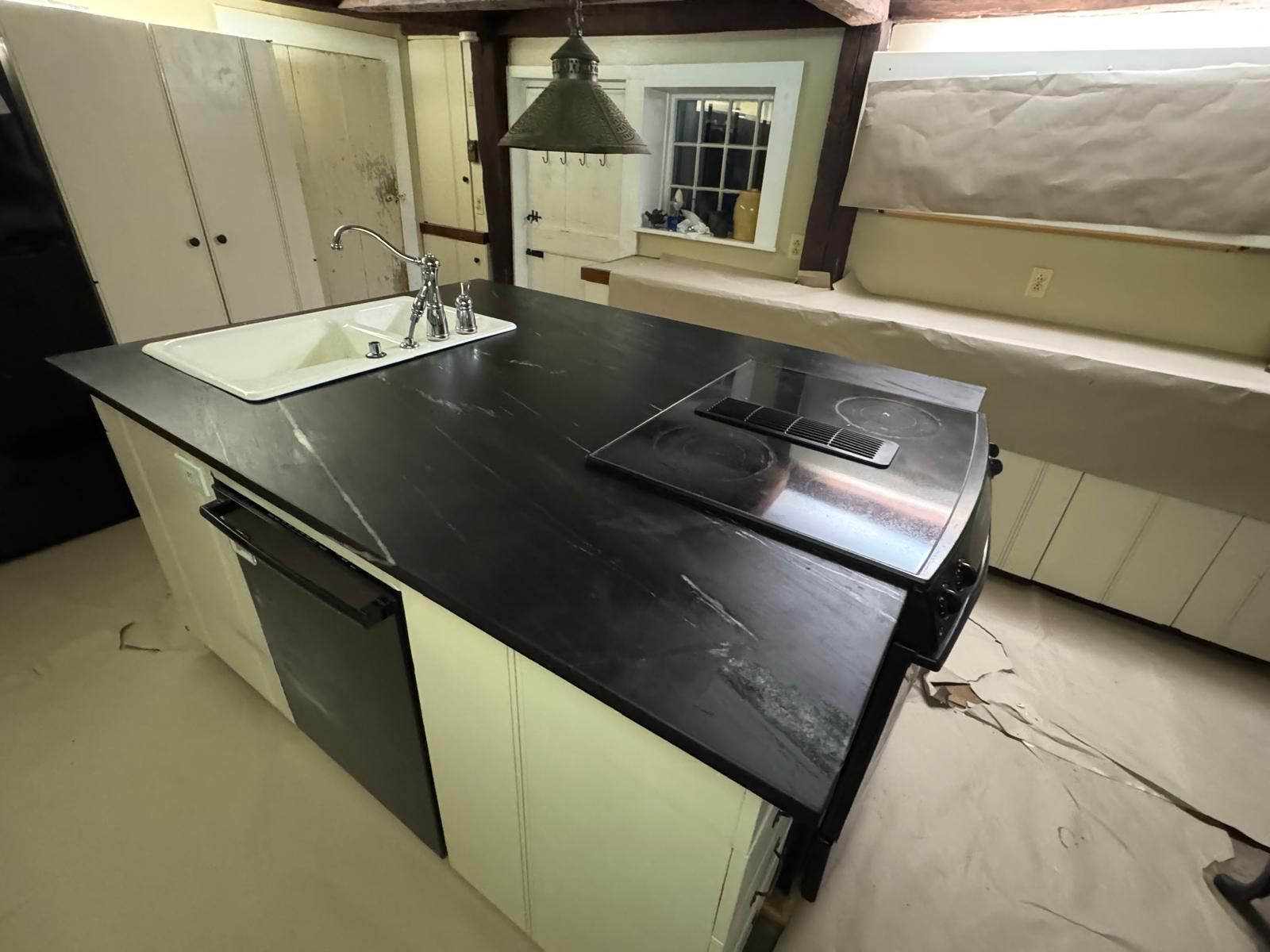 Kitchen island with black countertop, white cabinets, sink, and stovetop.