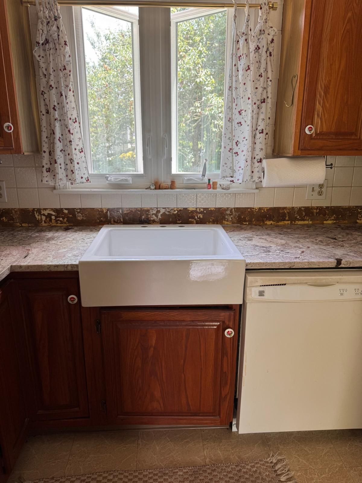 Kitchen with farmhouse sink, granite countertop, wooden cabinets, window with curtains, and dishwasher.