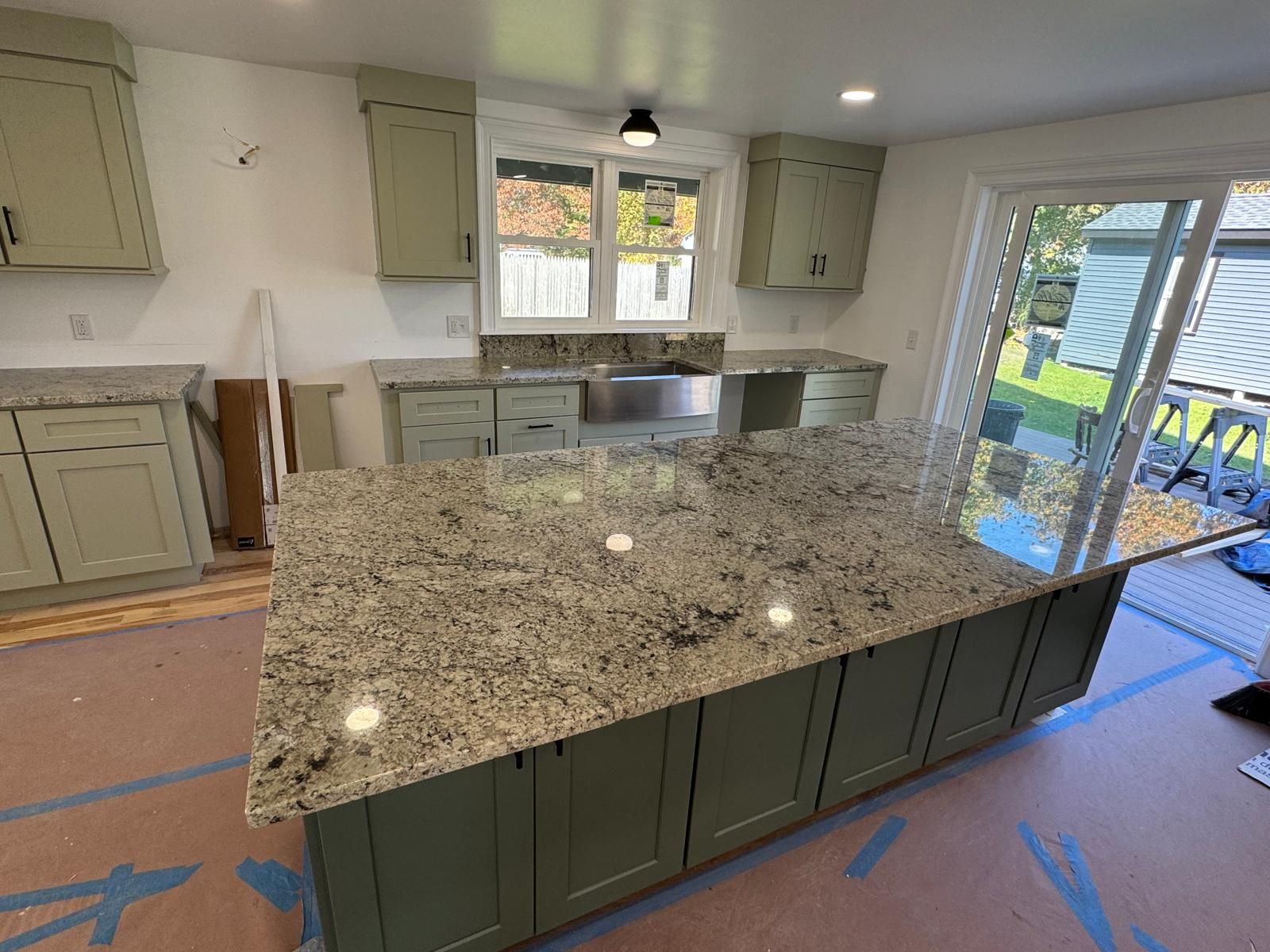 Green kitchen cabinets with granite countertops and a large island.
