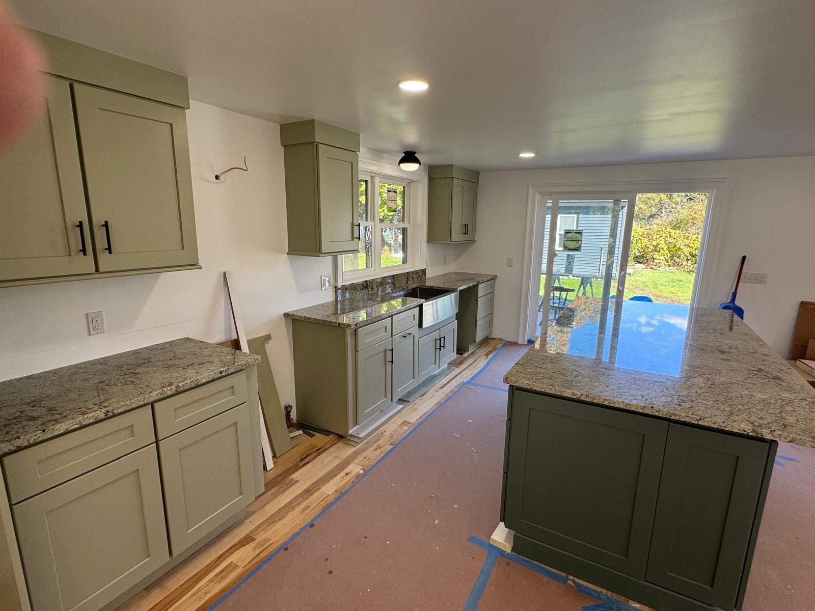 Kitchen under construction with sage green cabinets, granite countertops, and a sliding glass door.
