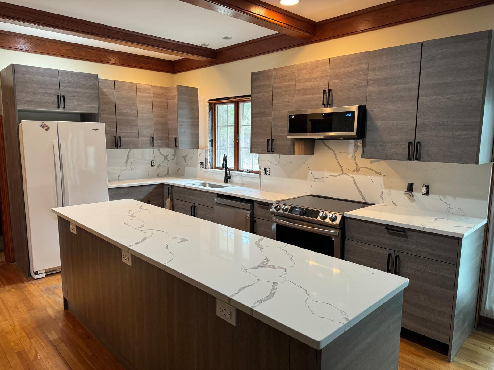 Modern kitchen with gray cabinets, white countertops, and wood flooring. Includes island and built-in appliances.