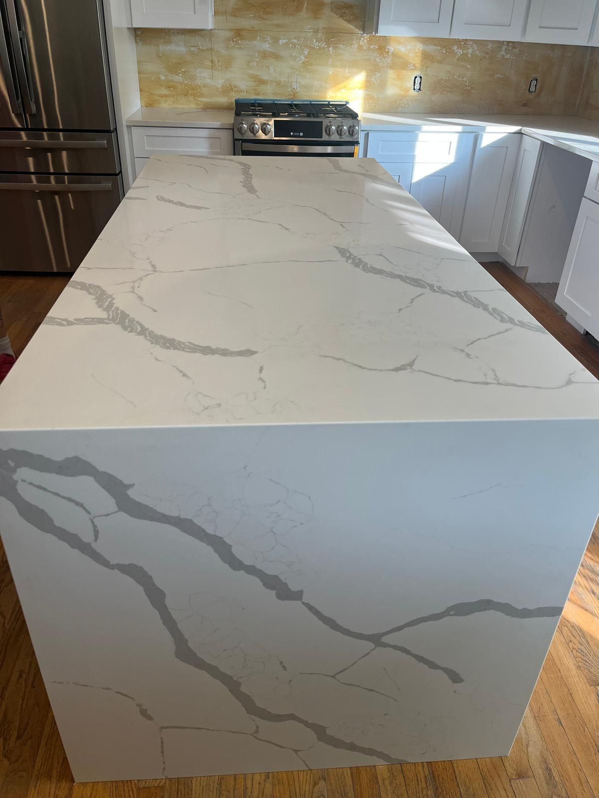 White kitchen island with gray veining. Stainless steel appliances and white cabinetry in the background.