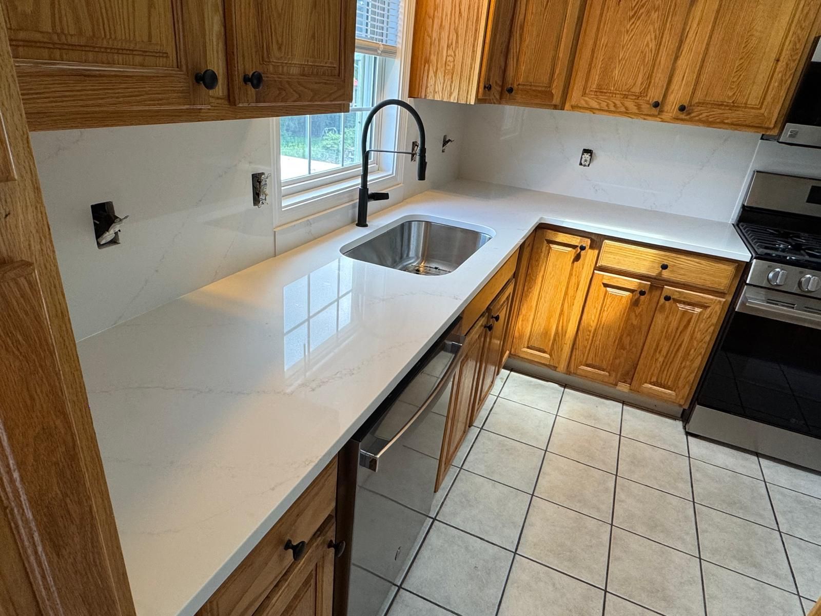 Kitchen with light countertops, oak cabinets, stainless steel sink and appliances.