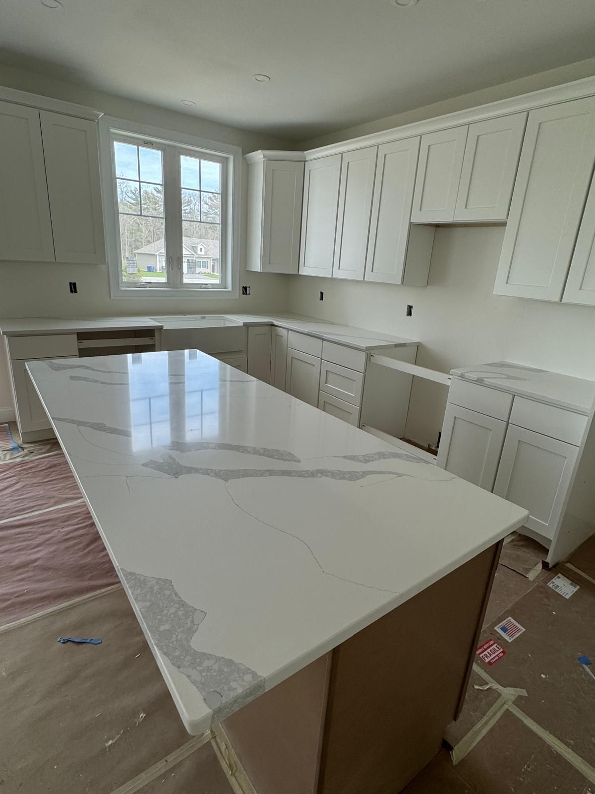 Kitchen with white cabinets, light countertops, and a large island. Window visible.