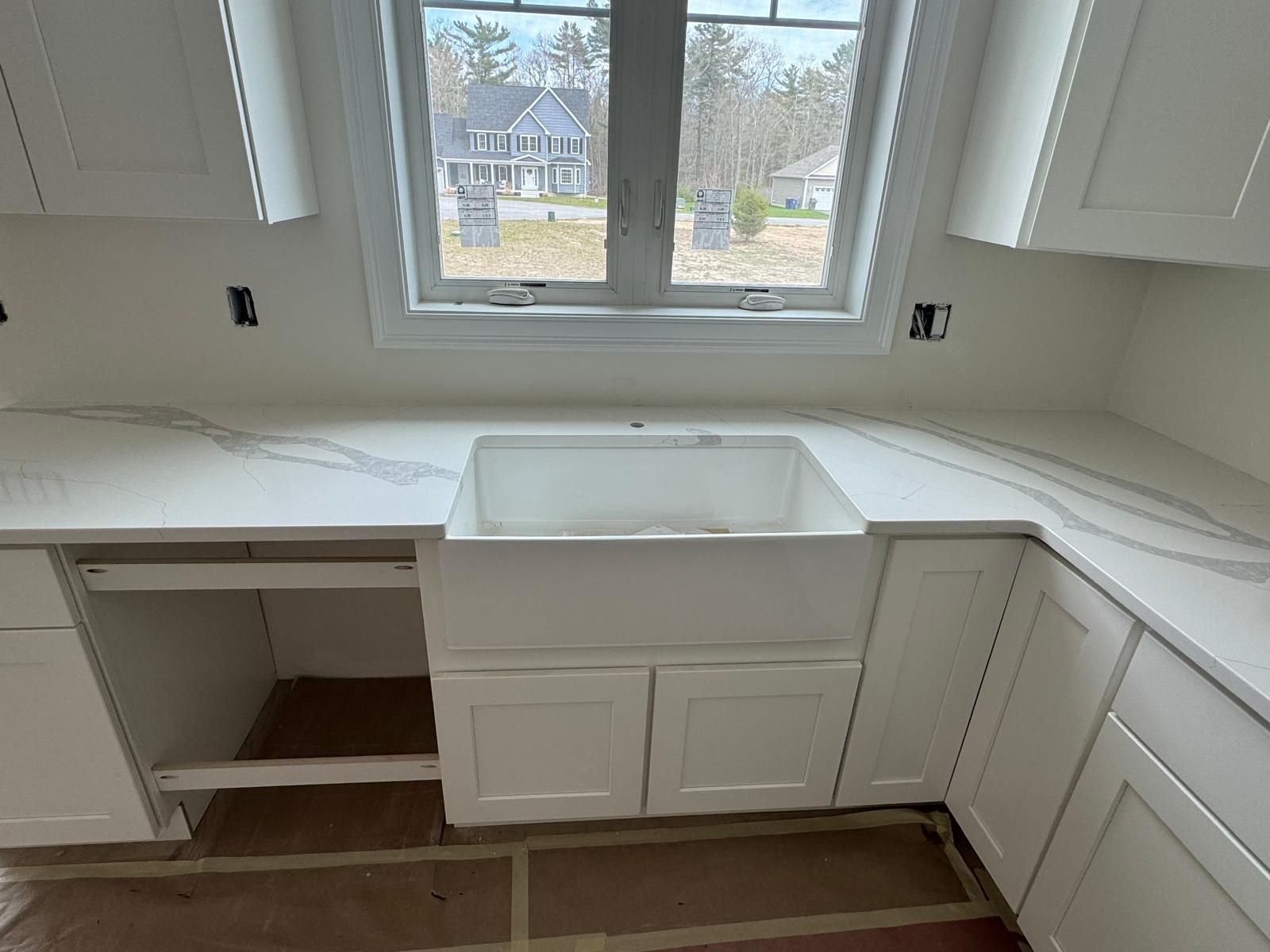 White kitchen with quartz countertop, farmhouse sink, and window overlooking a residential area.