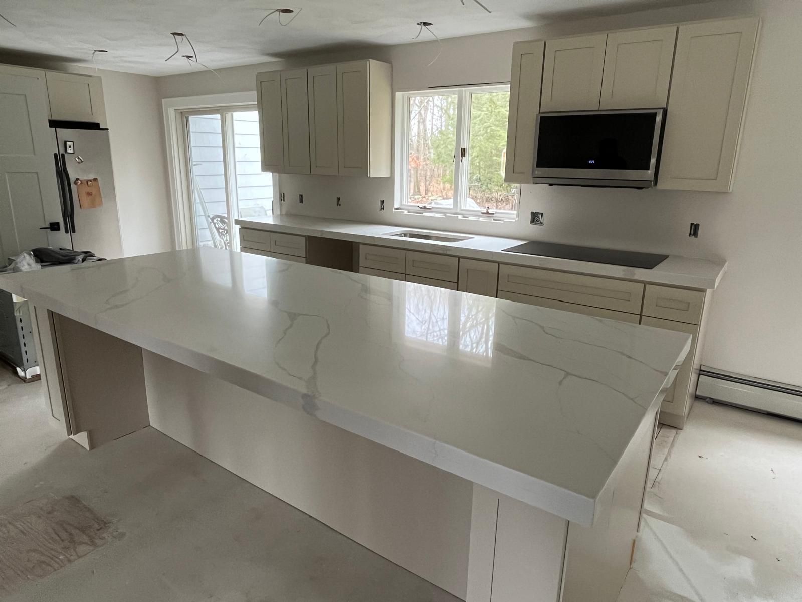 Kitchen with light cabinets and a large white island with a cooktop, still under construction.