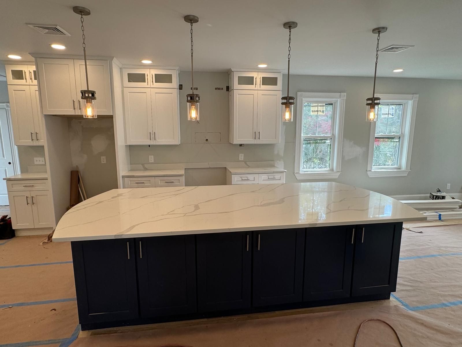 Kitchen with dark blue island, white cabinets, and pendant lights. Quartz countertop.