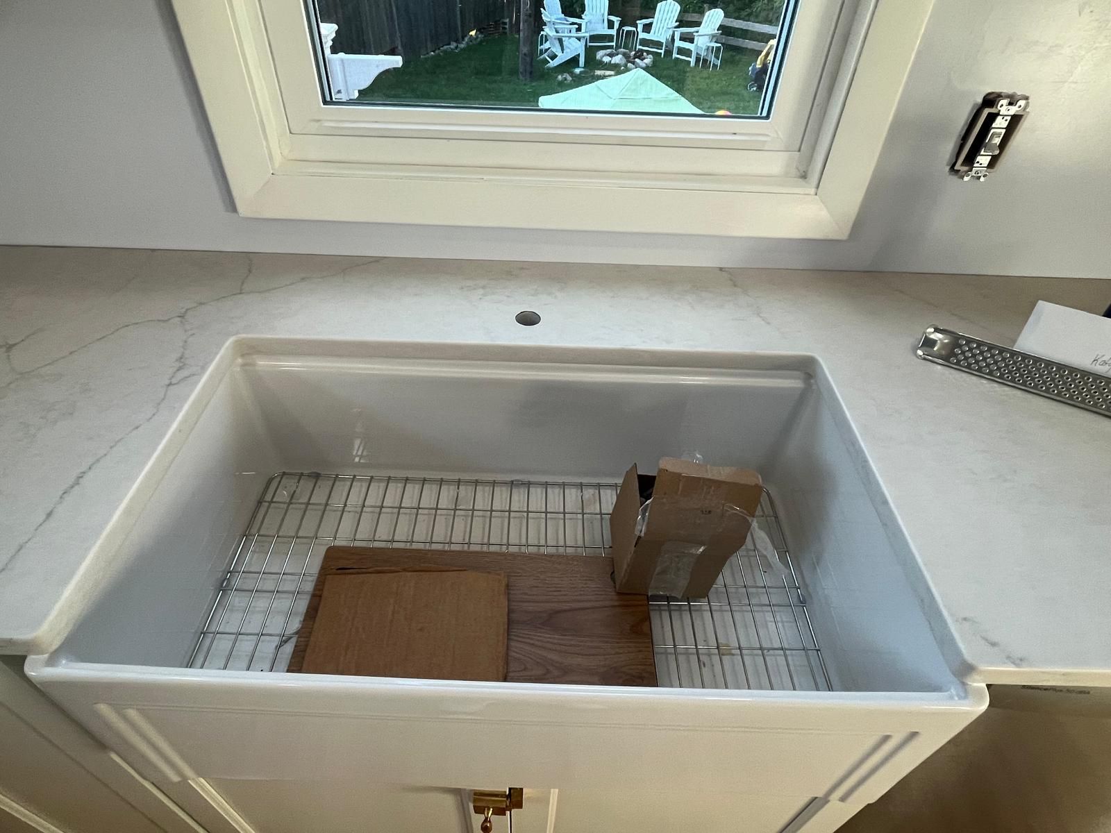 White farmhouse sink with cardboard inside, set in a kitchen with a window view.