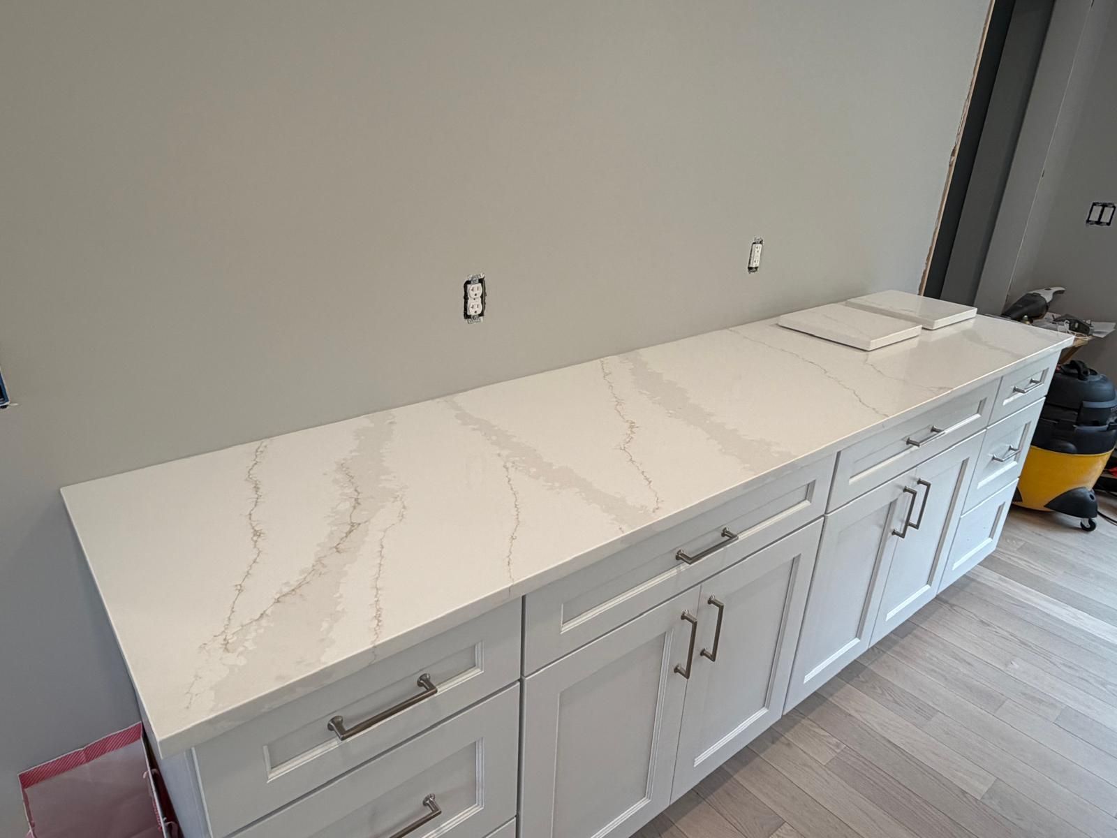 White kitchen cabinets with light countertops against a gray wall.