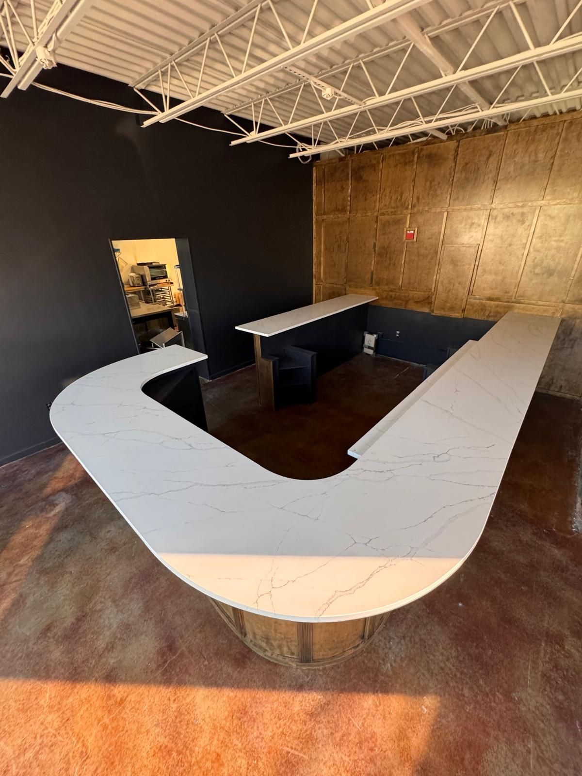 U-shaped white countertop in an unfinished interior with dark and tan walls.