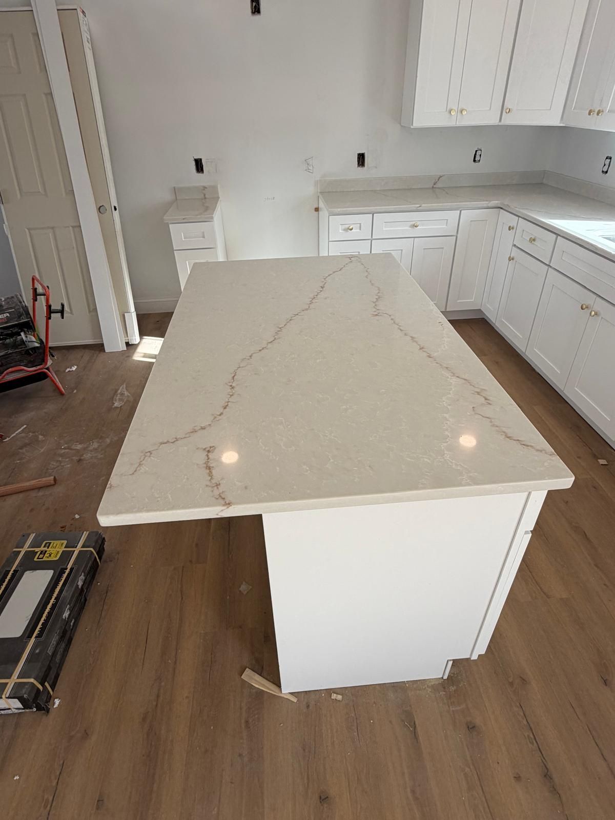 White kitchen with island and countertop with tan veining. Cabinets, wood floors, and neutral walls.