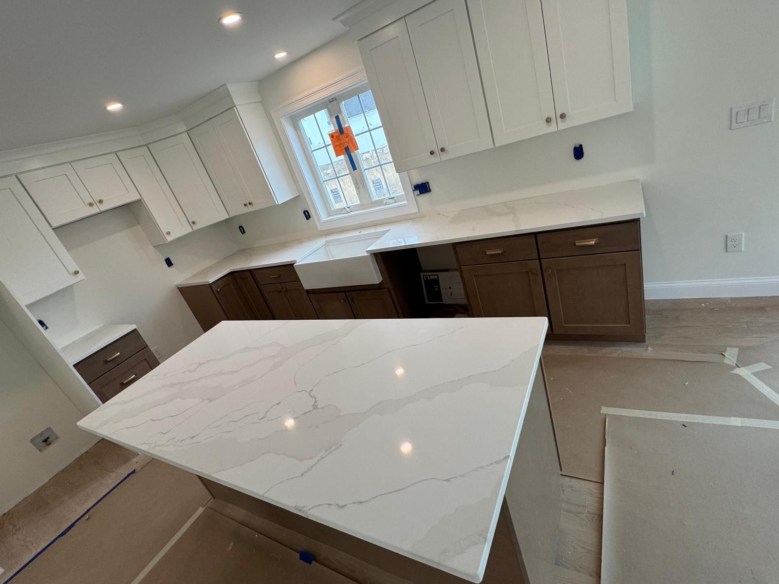 Newly renovated kitchen with white and brown cabinets, white countertops, and a central island.
